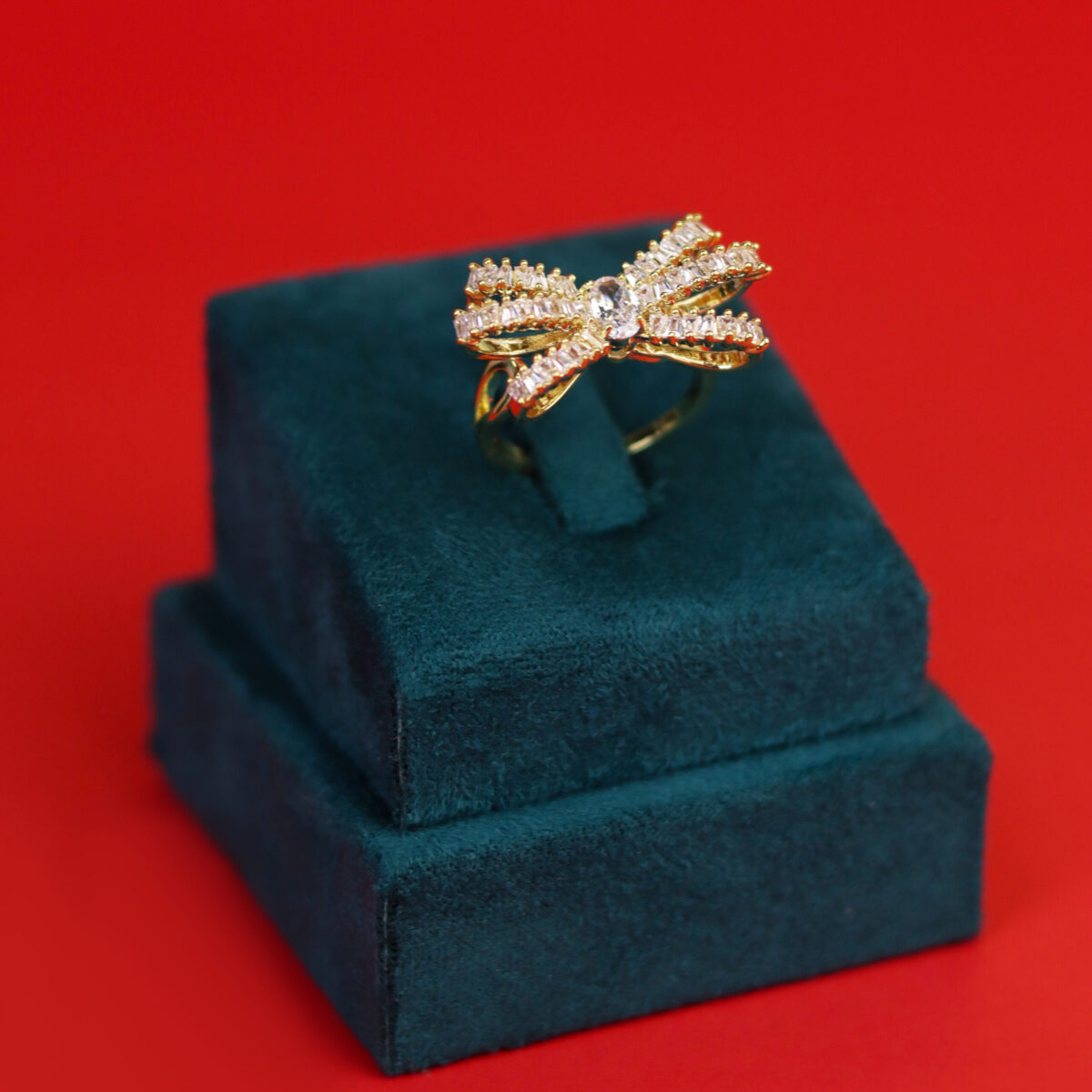 Gold ring shaped like a bow with diamond embellishments displayed on a velvet stand.