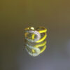 A yellow ring with a curved design and diamond embellishments reflecting on a surface.