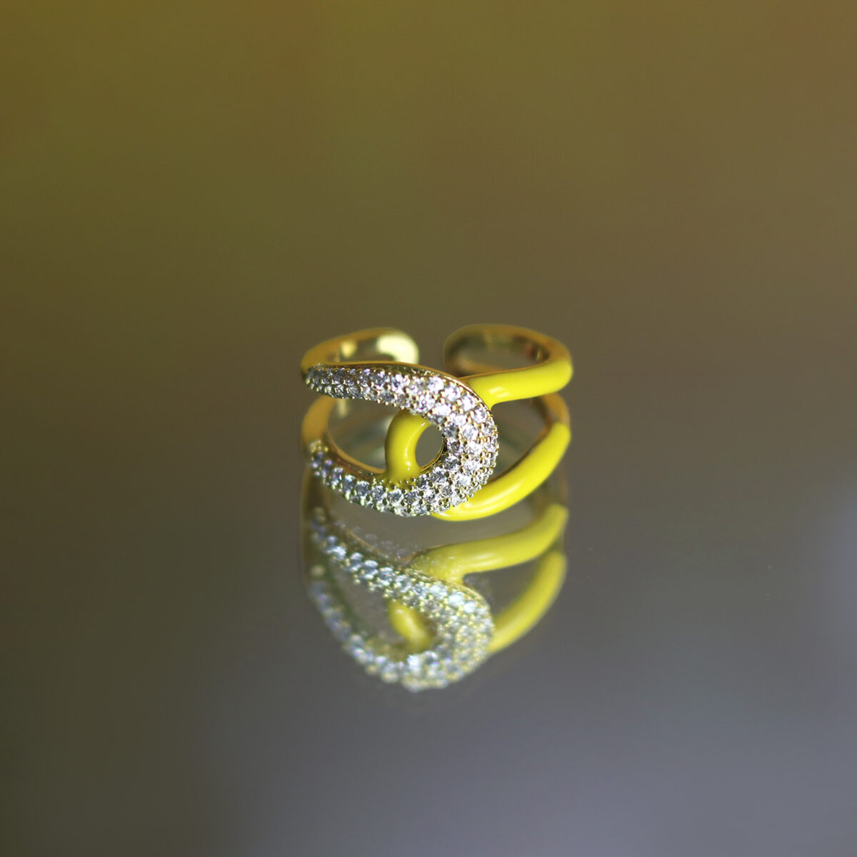 A yellow ring with a curved design and diamond embellishments reflecting on a surface.