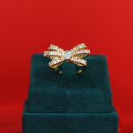 Gold ring shaped like a bow with clear stones set in a display box.