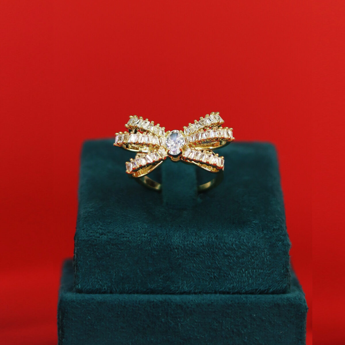 Gold ring shaped like a bow with clear stones set in a display box.