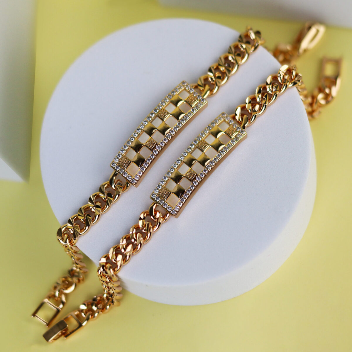 Two gold chain bracelets featuring a central design with diamond-like accents on a round display.