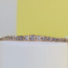 Gold bracelet with square-cut crystals arranged in a row on a white surface.