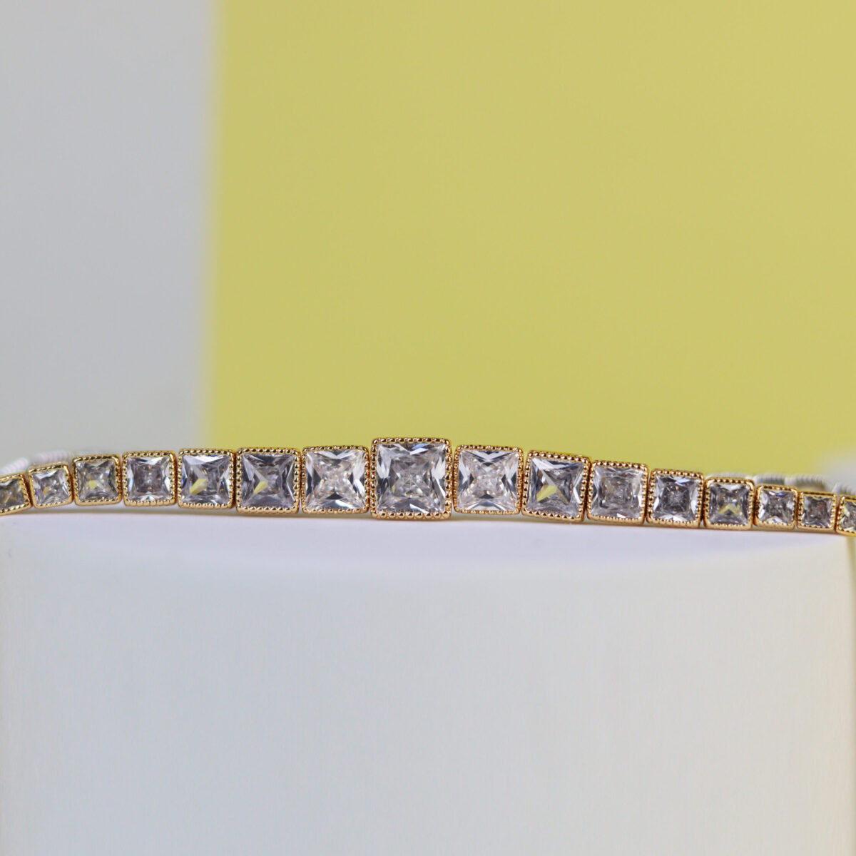 Gold bracelet with square-cut crystals arranged in a row on a white surface.