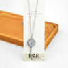 Silver key pendant necklace with a circular design and a large gemstone at the top, displayed on a card.