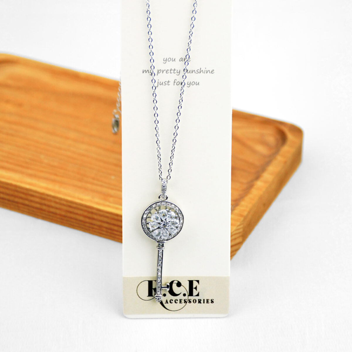 Silver key pendant necklace with a circular design and a large gemstone at the top, displayed on a card.