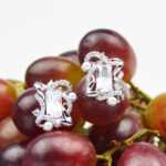 Silver earrings featuring clear rectangular crystals and pearl accents on a background of grapes.