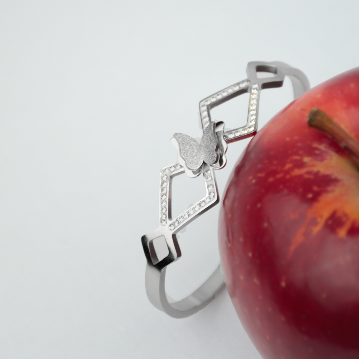 Elegant silver bracelet featuring a butterfly design adorned with sparkling diamonds, placed next to a red apple.